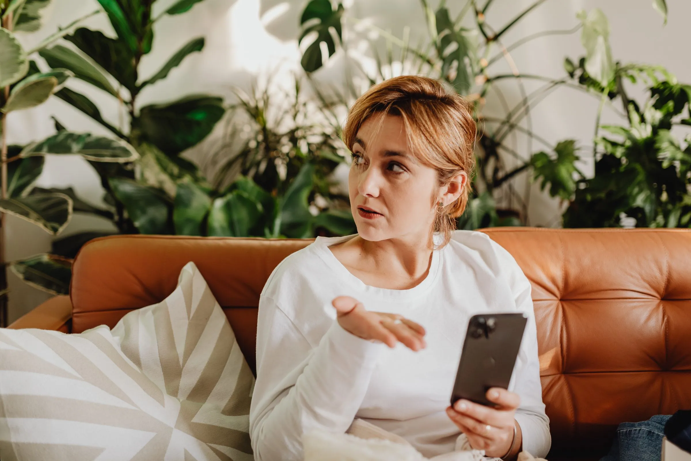 Femme qui pose une question sur son smartphone, assise dans un canapé