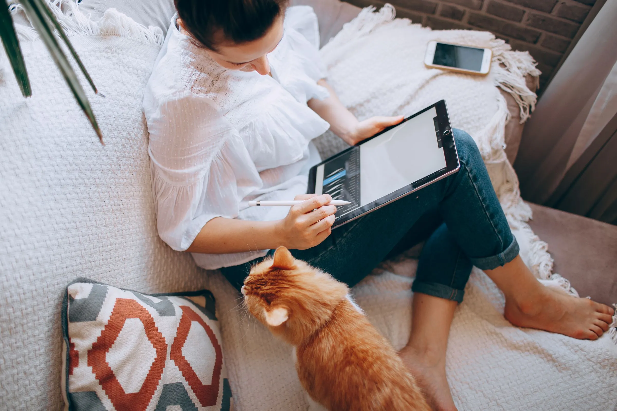 Femme qui lit sur une tablette, assise sur un canapé avec son chat