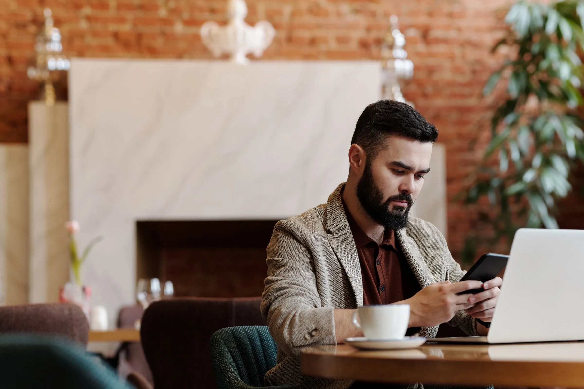 Homme qui consulte son smartphone devant son ordinateur dans un café